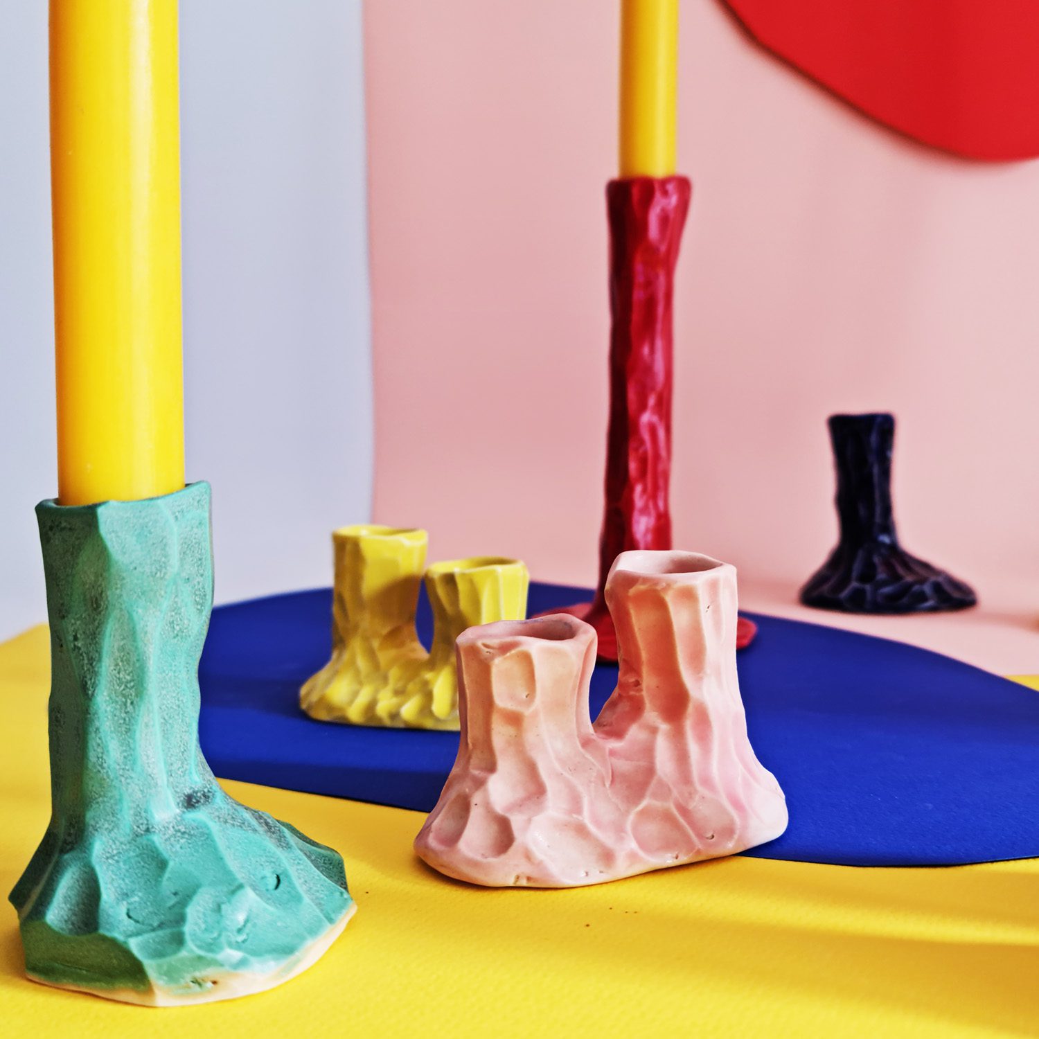 Colorful sculptural ceramic candlesticks with textured surfaces in bold tones, displayed on vibrant backgrounds.