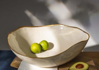 Porcelain bowl with an irregular gold-edged rim, styled with green speckled fruit and avocados on a wooden board