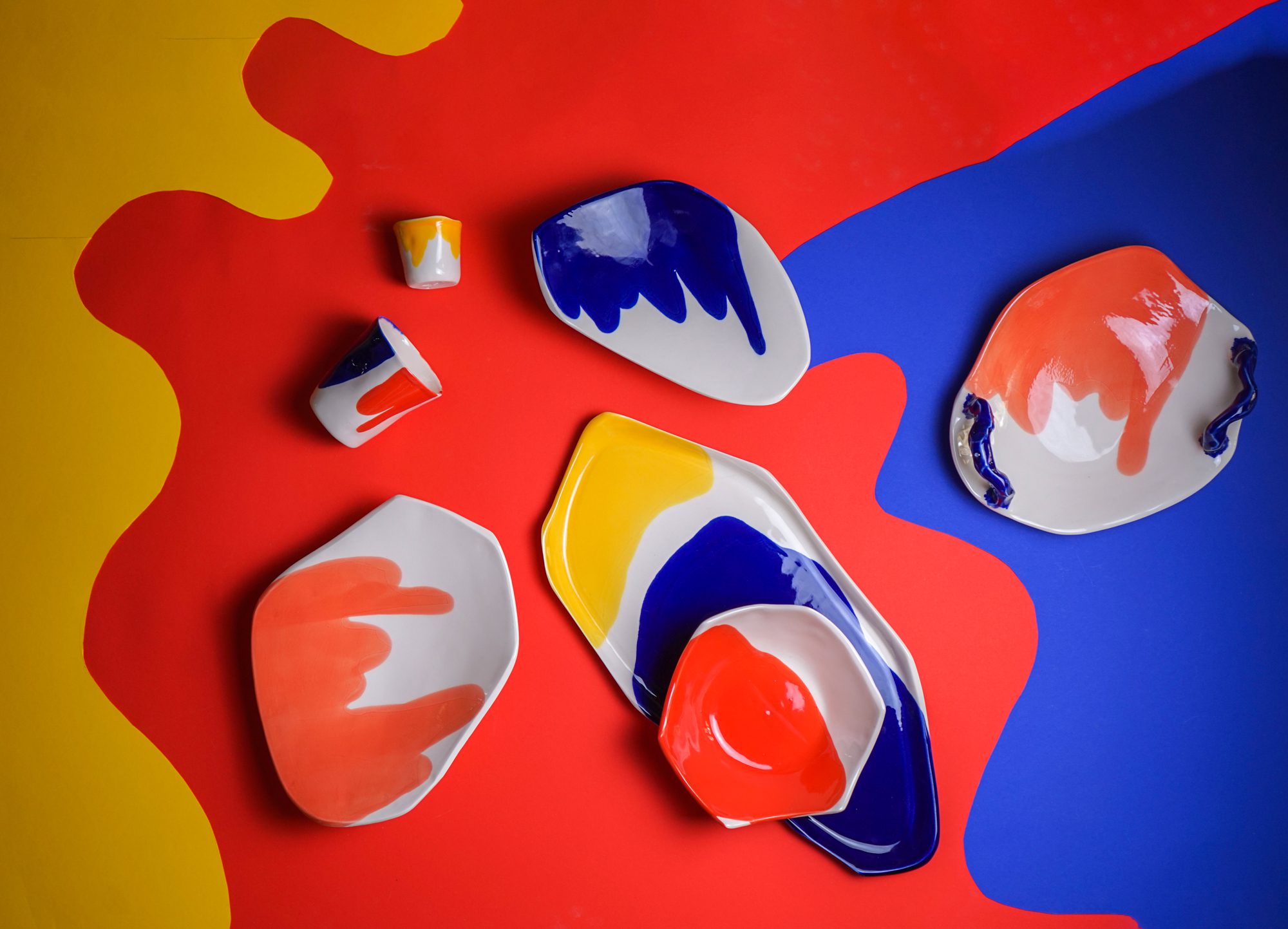 Multicolored porcelain plates and cups on a red, yellow, and blue abstract background.