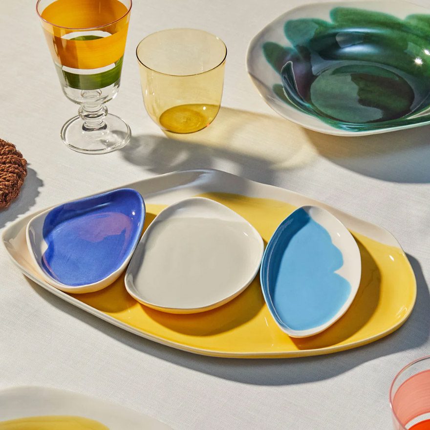 Colorful ceramic tray set with three small dishes in blue, white, and sky blue on a yellow base, styled on a dining table.